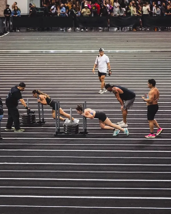 Athletes pushing weighted sleds on parallel lanes inside a large venue.