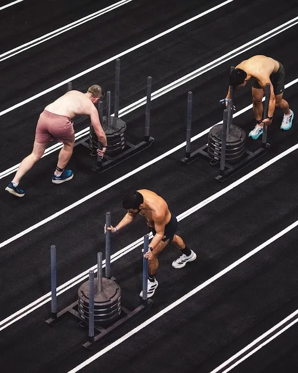 Overhead view of three athletes pushing weighted sleds along marked lanes.