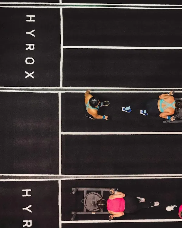 Overhead view of athletes and sleds on a grid of marked indoor lanes.