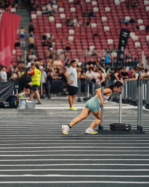 Athlete pushing a weighted sled along a marked indoor event lane.