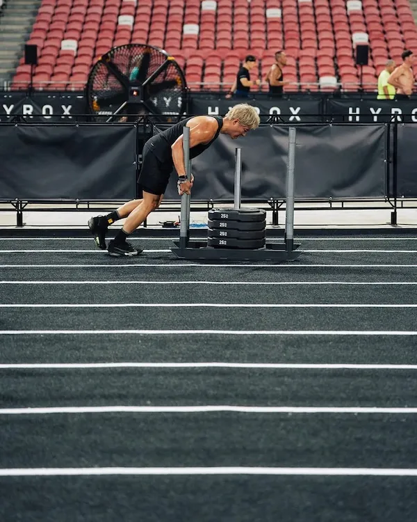 Athlete pushing a weighted sled across a marked indoor event surface.