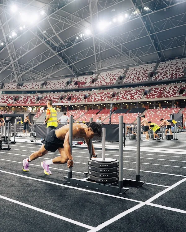 Athlete pushing a weighted sled on a marked lane inside a stadium.