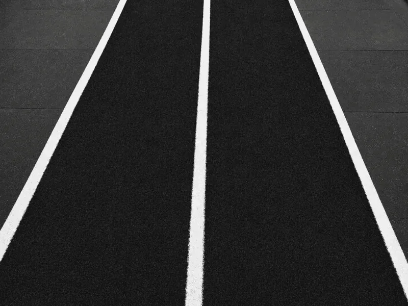 Simple green sled training turf with white parallel lane lines in a gym.
