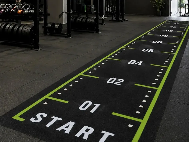 Green training turf with tufted distance numbers and lane markings in a commercial gym.